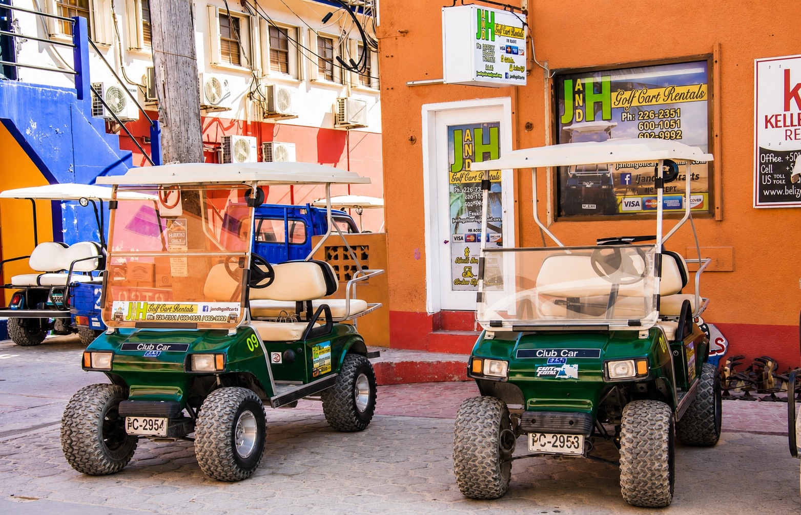 Two green J and H golf carts parked outside the J and H Golf Cart Rentals office on Barrier Reef Drive in San Pedro, Ambergris Caye, Belize